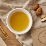 Huile d'amande douce bienfaits : huile, amandes et pipette sur tissu